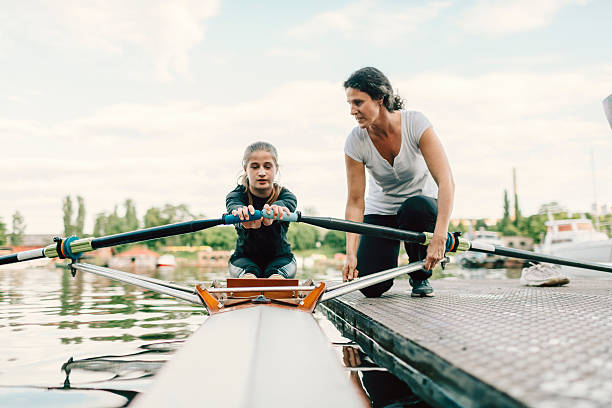 Une jeune fille apprend à ramer sous la supervision d’une coach sur un ponton.